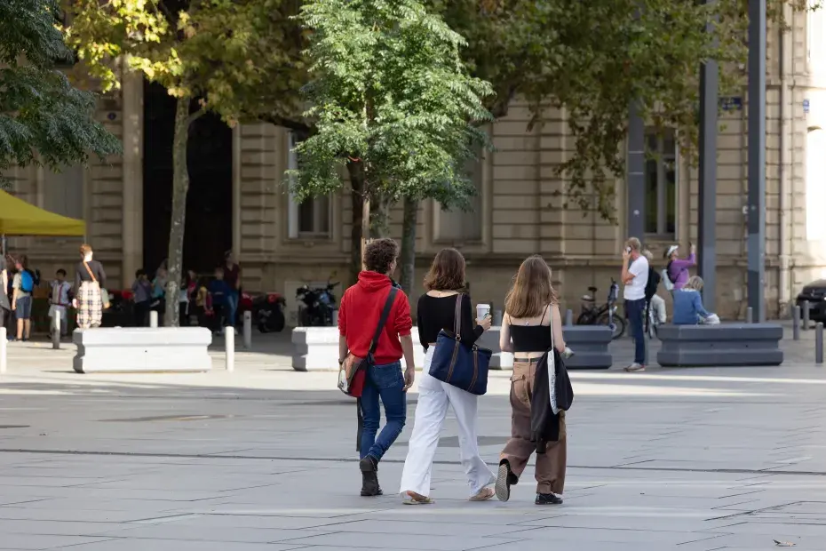 Un groupe de trois personnes composé d'un homme et deux femmes marchent sur la place Pey-Berland à Bordeaux.